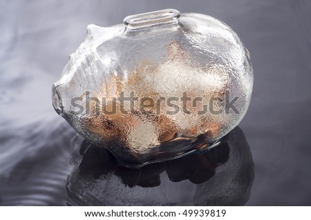 a glass piggy bank with coins reflecting on a water base background