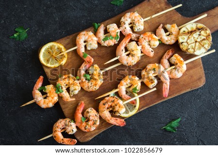 Grilled shrimp skewers. Seafood, shelfish. Shrimps Prawns skewers with herbs, garlic and lemon on black stone background, copy space. Shrimps prawns brochette kebab. Barbecue srimps prawns.