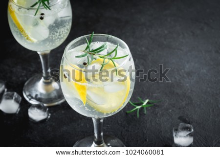 Alcohol drink (gin tonic cocktail) with lemon, rosemary and ice on rustic black stone table, copy space, top view. Iced drink with lemon.