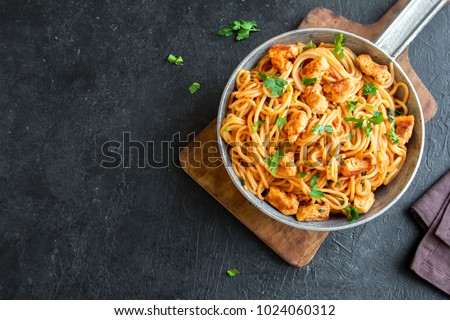 Spaghetti pasta in tomato sauce with chicken,  parsley in pan. Chicken spaghetti pasta over black stone background with copy space, italian food.