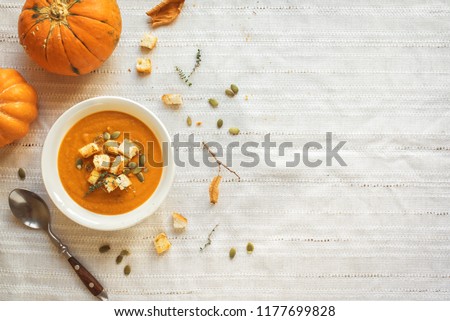 Pumpkin soup and organic pumpkins, top view, copy space. Seasonal autumn food - Spicy pumpkin soup with croutons and pumpkin seeds.