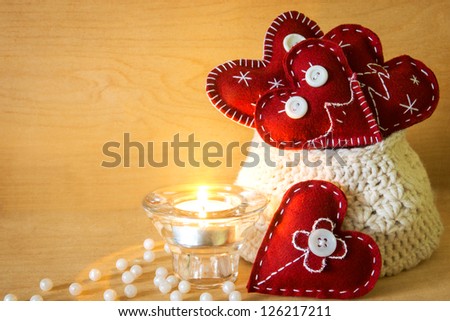Valentine\'s Day concept. Red handmade hearts in knitted bag, candle and pearls on wooden texture