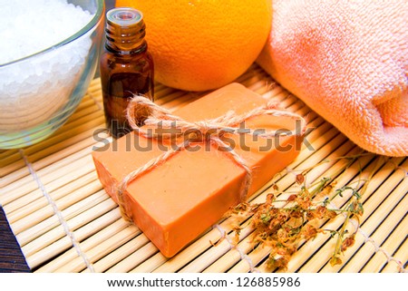 Natural handmade soap, essential oil, dried herbs, bath salt, orange and towel on bamboo mat. Spa concept.