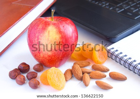 Healthy quick snack (lunch) in office. Red apple, dry fruits (apricots) and nuts on desk with computer and planner.