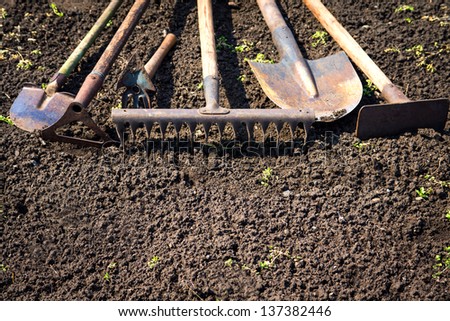 Old retro garden tools (cultivator, shovel, rake) over brown soil (ploughed land) close up. Copy space. Agriculture, gardening, soil cultivation concept.