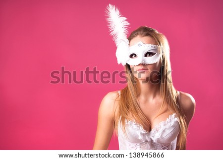 Beautiful sexy sensual pretty young woman in white lace underwear and mask with feather over pink background. copy space