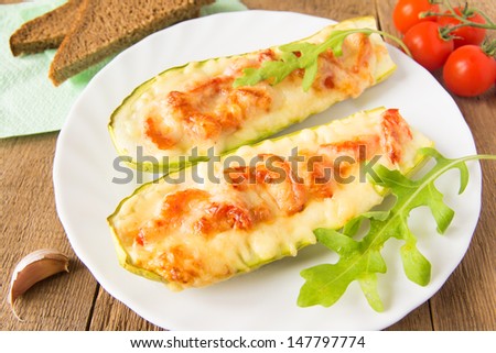 Stuffed fresh homemade zucchini with tomatoes, garlic and cheese on wooden background with argula leaves and bread, close up, horizontal. Natural vegetarian dinner concept.