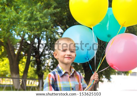Beautiful happy cute joyful smiling blond child (little boy) with bunch of balloons in hands, close up outdoor portrait, birthday, fun and summer holiday.