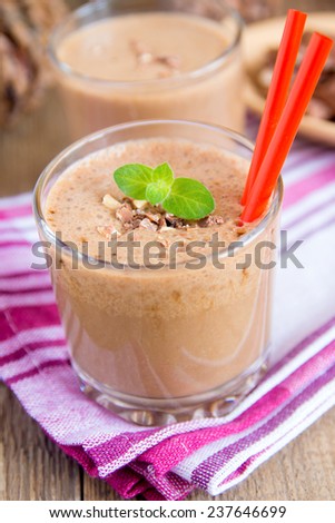 Milkshake (chocolate and banana smoothie) in glass with mint and nuts, homemade dairy breakfast or dessert vertical close up