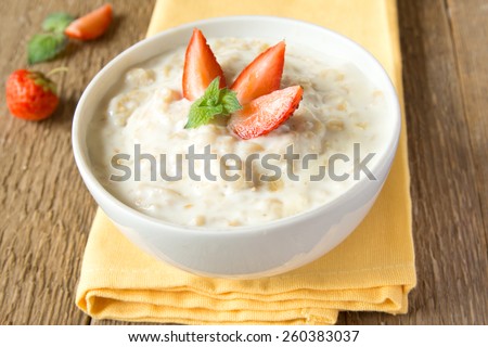 Fresh hot oatmeal porridge with berries and mint on napkin and wooden table, close up, horizontal, copy space. Healthy vegetarian summer breakfast.