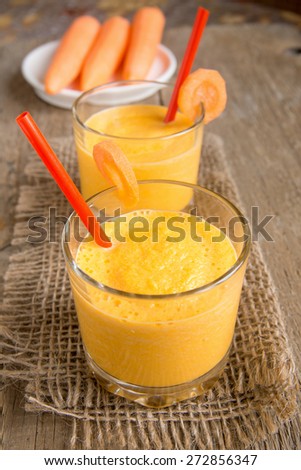 Carrot smoothie on wooden background, vertical close up
