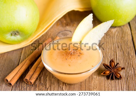 Fresh homemade applesauce (apple puree, babyfood) with cinnamon (spices), spoon and apples on wooden table close up, vertical