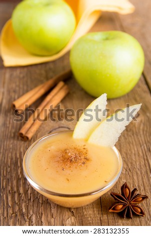 Fresh homemade applesauce (apple puree, mousse, baby food) with cinnamon (spices), spoon and apples on wooden table close up, vertical