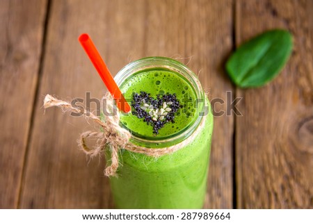 Green vegetable and herbs smoothie with heart of poppy and sesame seeds in jar over rustic wooden background