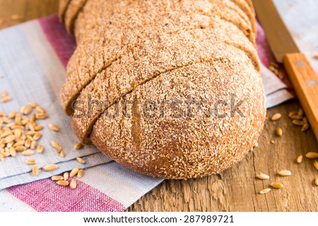 Wholegrain bread with wheat grains on linen napkin and rustic wooden background (table)