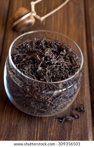 Black dried tea leaves in glass jar on wooden background