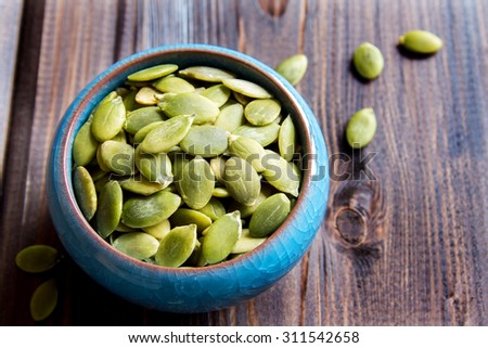 Pumpkin seeds in blue bowl over wooden background close up