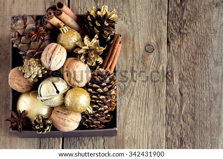 Christmas golden decoration -  cones, ornaments, nuts and spices in box over rustic wooden background with copy space