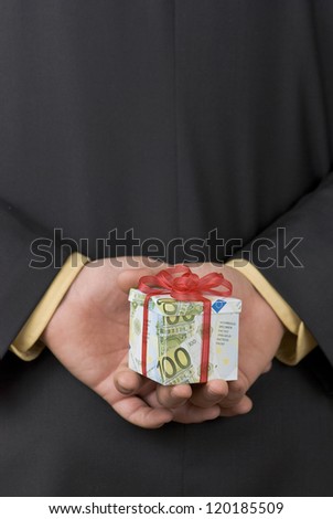 Man holding an expensive gift box wrapped in euro banknotes behind his back