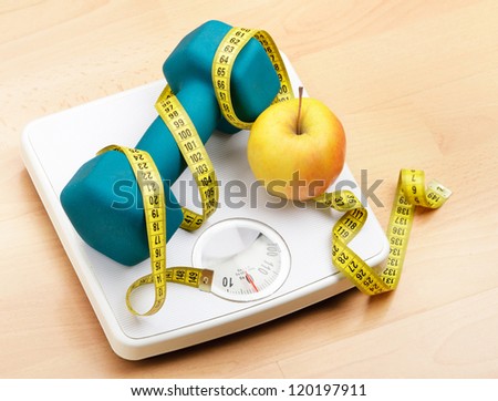 Fresh apple and dumbbells tied with a measuring tape on a weighting scale