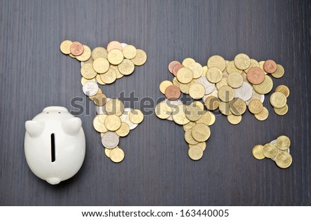 Office desk with world map made of money coins and piggy bank