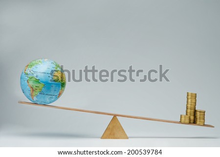 World globe and money coins stack balancing on a seesaw
