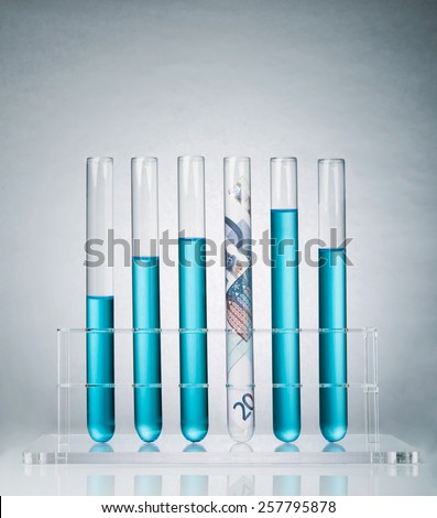 Rolled up Euro paper banknote in a test tube rack representing the costs of medical research