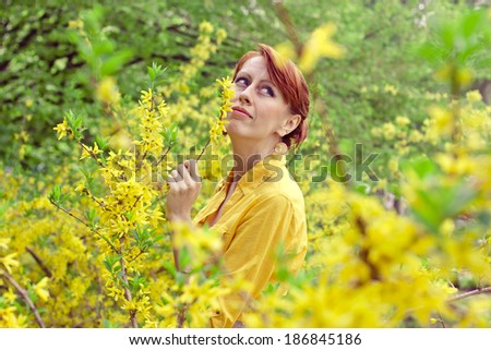 red-haired girl in a yellow shirt near the bush with yellow flowers