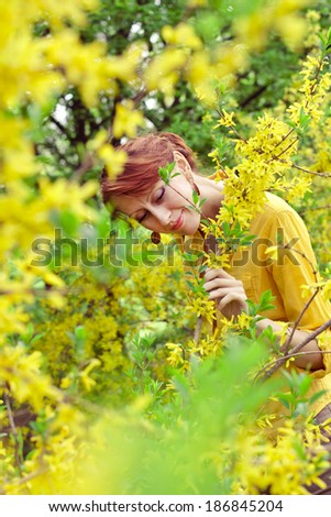 red-haired girl in a yellow shirt near the bush with yellow flowers