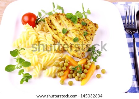 Grilled turkey steak with noodles peas, carrots, tomato and oregano, top view