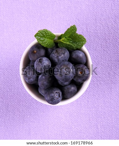 Blueberries with mint in white bowl on purple background, top view