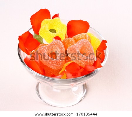 Two red hearts candies in glass bowl and rose petals, close up