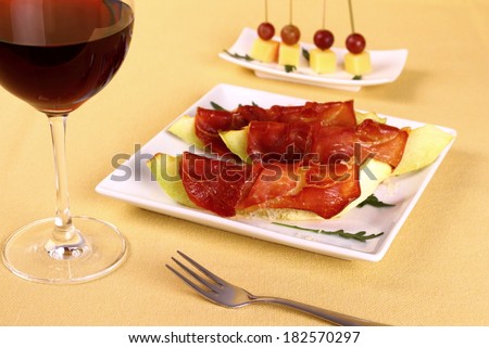 Baked melon with proscuitto ham, parmesan on white plate, red wine