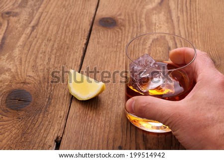 Whiskey with ice cubes in glass withnd grab hand, close up