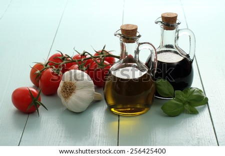 Olive oil and vinegar in vintage bottles on wooden table, cherry tomatoes with garlic