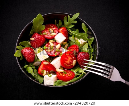 Strawberry tomato salad with feta cheese, olive oil on black background