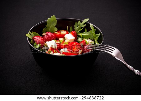 Strawberry tomato salad with feta cheese, fork on black background