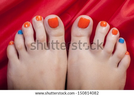 Close-up shot of beautiful woman feet with red and blue pedicure on the red
