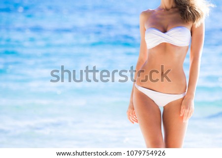 Tanned woman body in white bikini, blue sea water in background