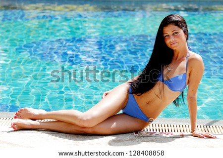 Young sexy woman sitting on the ledge of the swimming pool