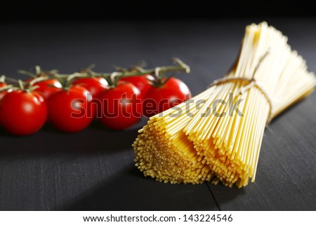 Raw pasta and tomatoes on black table close-up