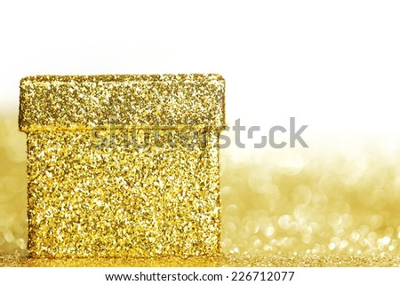 Decorative golden box with holiday gift on shiny glitter background