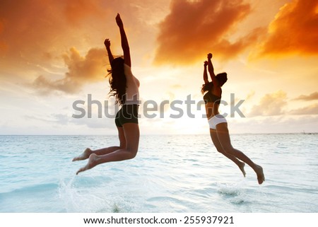 Two happy women jumping on sunset beach near sea