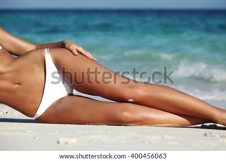 Woman with perfect body in bikini lying on beach over blue sea background