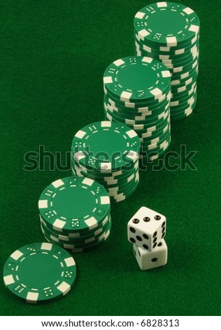 Crescent piles of green poker chips over a green table and besides two white dice.