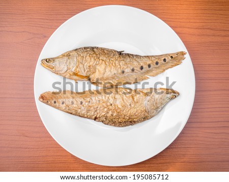 dry grilled smoked featherback fish ( preserve food ) on white dish on wood background