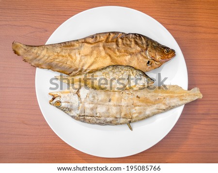 dry grilled smoked featherback fish ( preserve food ) on white dish on wood background