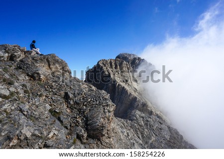 Woman sitting of the summit of Skala looking towards the summit of Mytikas, Greece, Mount Olympus