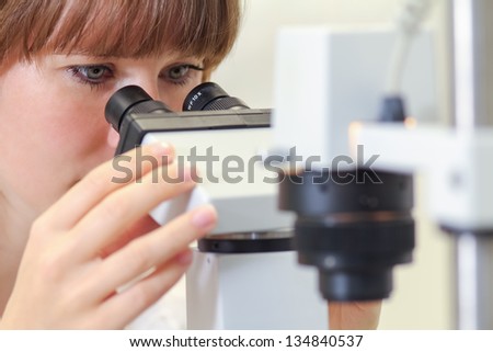 A young female scientist working in cancer research is looking through a microscope at cells.