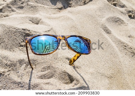 Sunglasses on beach sand which reflects the sun and umbrellas